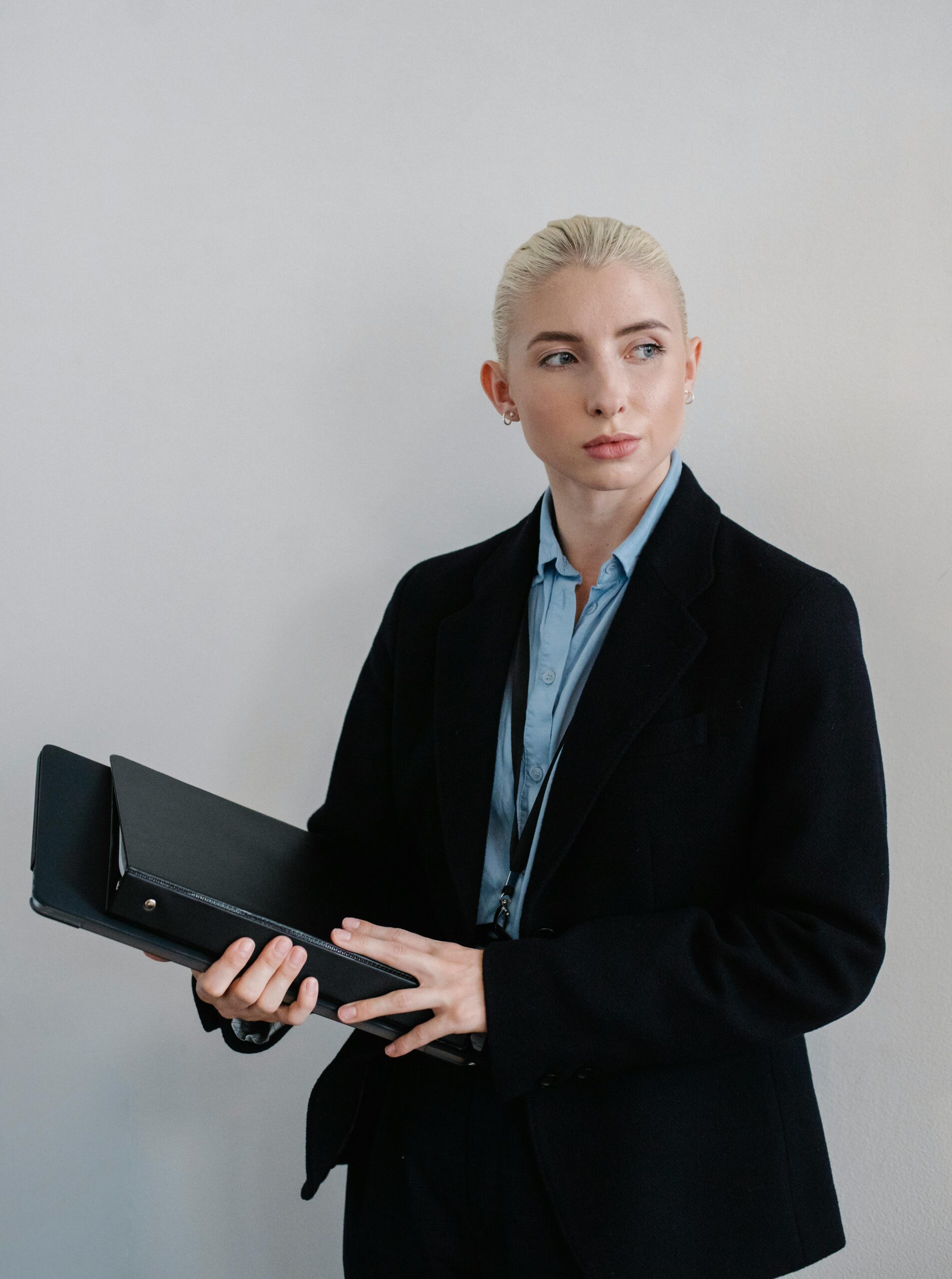 Confident businesswoman in a corporate setting holding a folder, looking thoughtfully to the side.