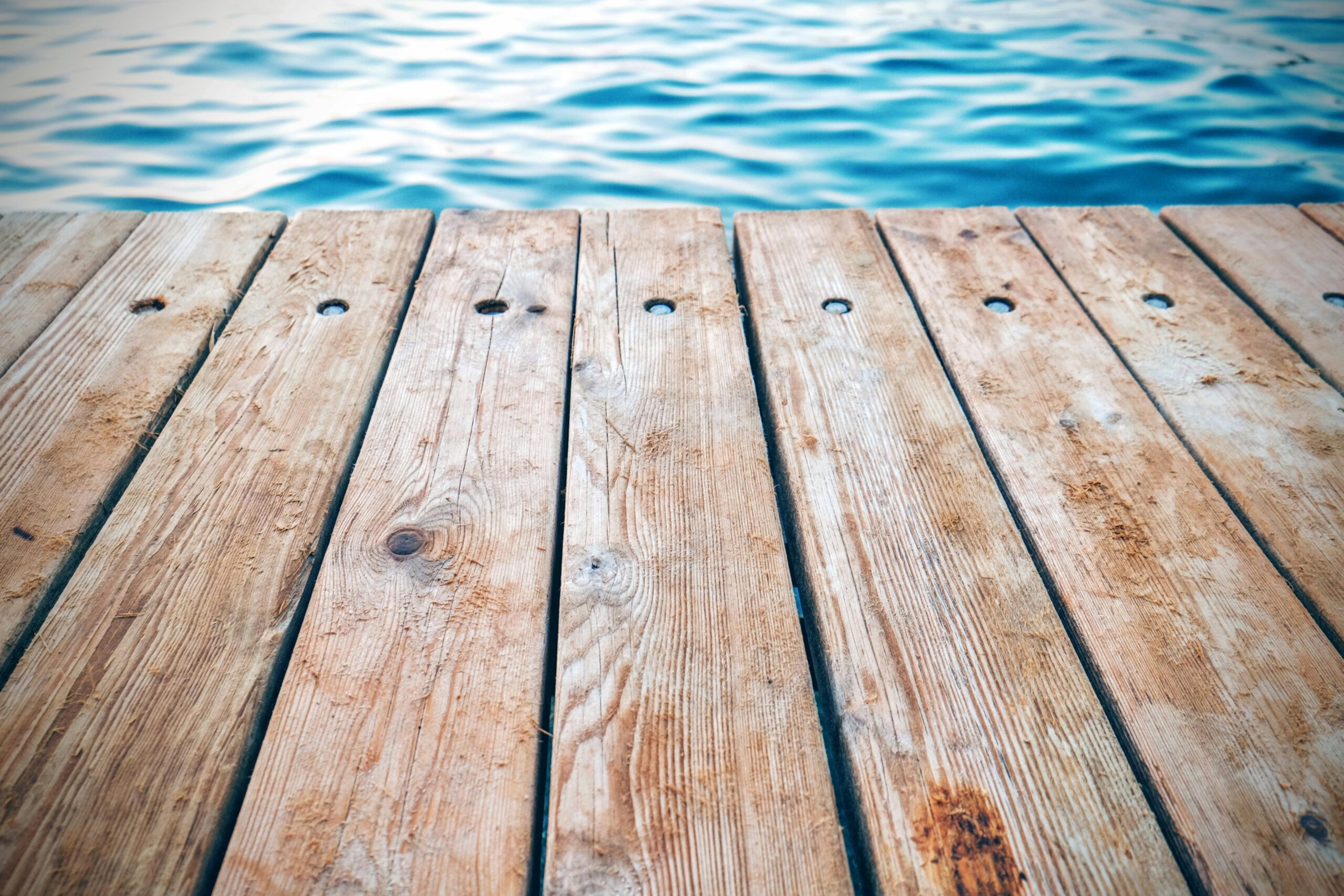 A detailed view of a rustic wooden pier with textured planks by calm blue water. Perfect for serene and nature themes.